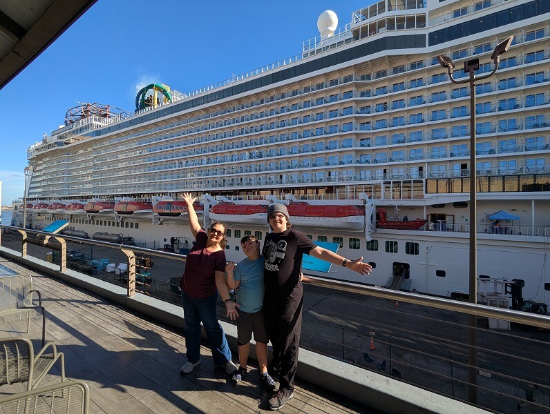 Cruises from New Orleans - Mother and two sons stand on a balcony with a cruise ship in the background